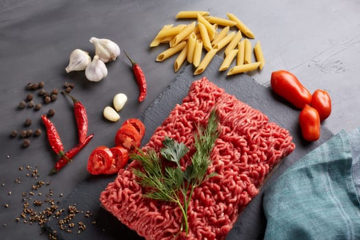 Still life with fresh forcemeat from beef, vegetables, pasta and spices on a dark background. Top view