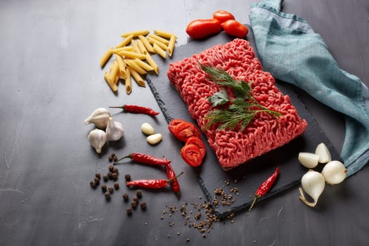 Still life with fresh forcemeat from beef, vegetables, pasta and spices on a dark background. Top view