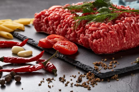 Still life with fresh forcemeat from beef, vegetables, pasta and spices on a dark background.