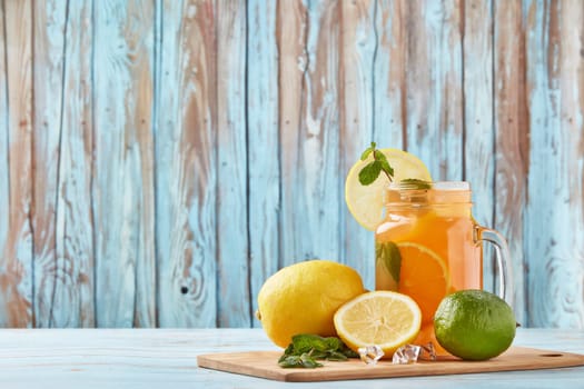 Citrus lemonade with ice, leaves of mint, lemon and lime slices standing on blue wooden table. Homemade lemonade with citruses. Healthy cool beverage