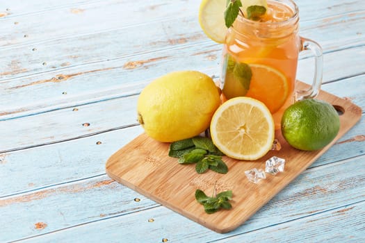 Citrus lemonade with ice, leaves of mint, lemon and lime slices standing on blue wooden table. Homemade lemonade with citruses. Healthy cool beverage