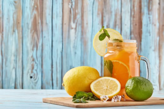 Citrus lemonade with ice, leaves of mint, lemon and lime slices standing on blue wooden table. Homemade lemonade with citruses. Healthy cool beverage
