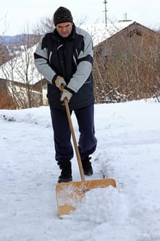 A man shovels snow from a sidewalk in the winter.