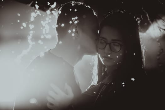 black white photo young couple standing under a dark umbrella.