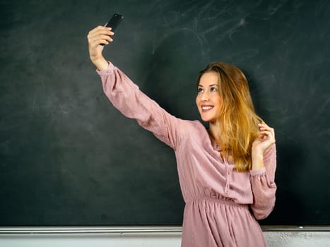 Photo of a beautiful student in a classroom doing a selfie in front of a blackboard.