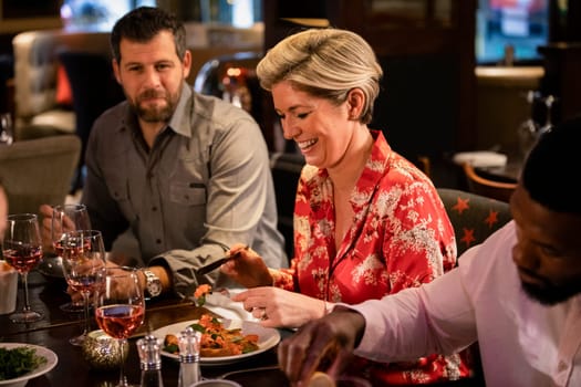 Mature woman sitting at a table in a restraurant with friends while enjoying her food.