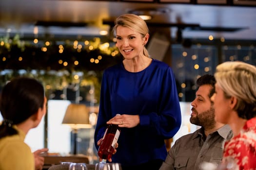 Female waitress reccomending a bottle of wine to two couples while sitting in a restaurant.