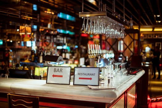 Interior shot of a restaurant bar counter which has signs pointing to either the bar or the restaurant.