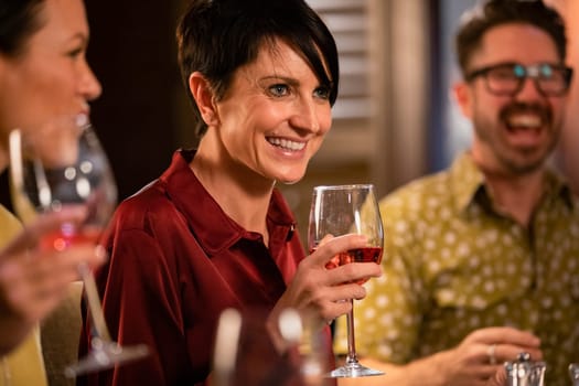 Close-up of a mature woman holding a glass of rose wine. She is smiling and talking with friends in a restaurant.