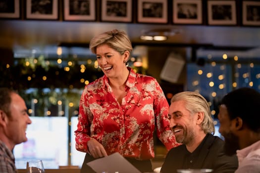 Smiling mature waitress taking an order of food from a small group of mid adult men in a restaurant.