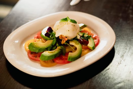 Fresh avocado and mozzarella salad on a plate on a wooden table in a restaurant.