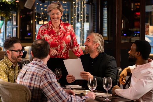 Female waitress standing at the edge of the table as she waits for a group of mid adult men to order some food.