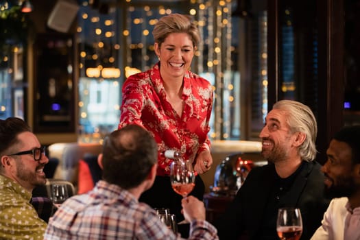 Female waitress standing at the edge of the table as she pours a glass of rose wine for a mature adult man.