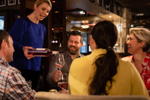 Over the shoulder view of two couples sitting at a table in a restaurant. The waitress is pouring a glass of while while a mature male holds the glass.
