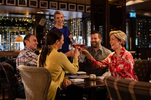 Two mature couples making a celebratory toast with a glass of rose wine while sitting in a restaurant.