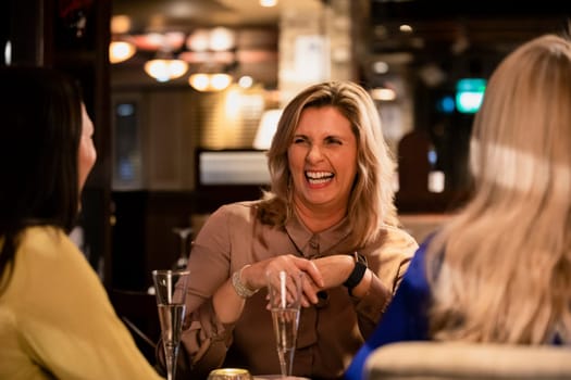 Over the shoulder view of a mature woman laughing and smiling with her friends while sitting in a restaurant.