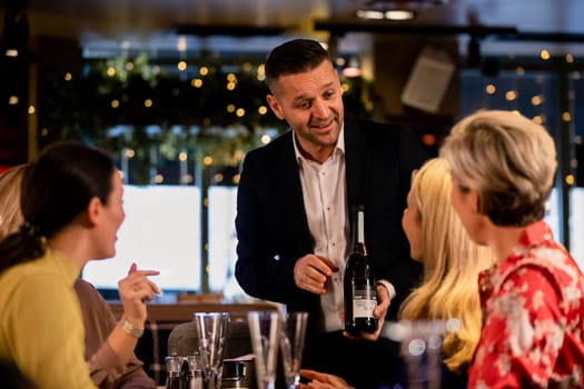 Mature wiater offering and showing a small group of mature women what type of prosecco they offer at the restaurant.