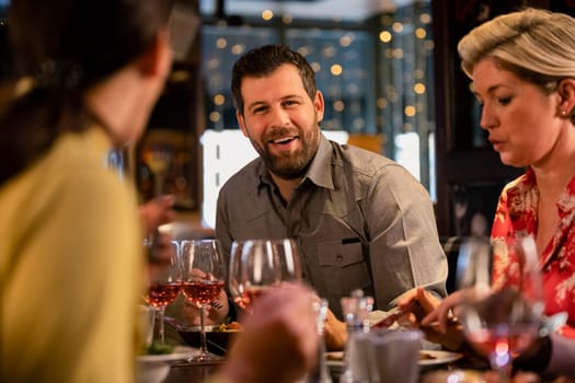 Mid adult man sitting at a restaurant table with some friends and enjoying a meal.
