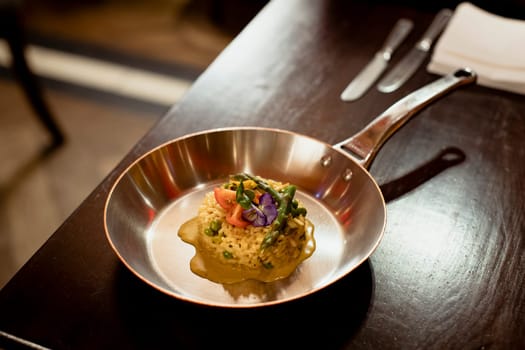 Restaurant style risotto dish presented in a silver frying pan on a wooden table in a restaurant.