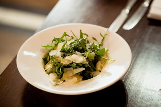 Restaurant style parmesan and rocket salad presented in a bowl on a wooden table in a restaurant.