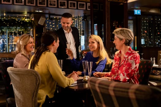 Mature woman making a celebratory toast while sitting around a table in a restaurant with her friends. There is awaiter pouring a glassses of prosecco.