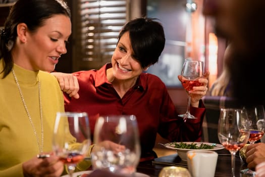 Two mature women enjoying a glass of rose wine with their meal. They are laughing and smiling while talking.