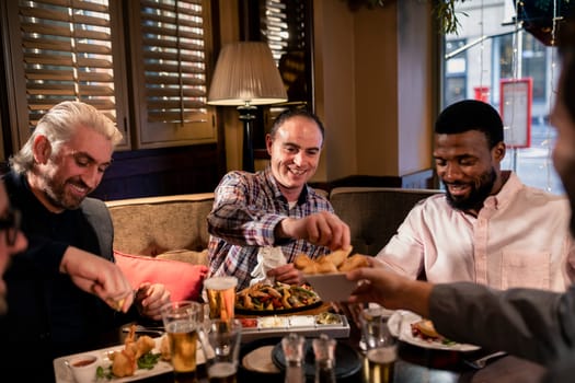 Small group of mid adult men enjoying some food. One man has been offered a chip by one of his friends.