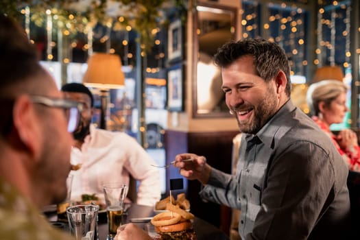 Small group of mid adult male friends enjoying some food in a restaurant. They are talking and enjoying each others company.