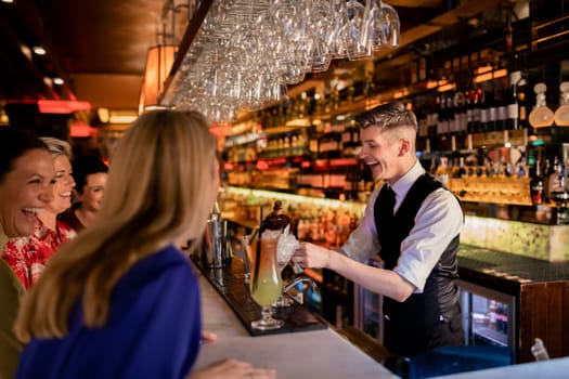 Young bartender making a cocktail for a small group of women enjoying ladies night. They are all laughing and making conversation.