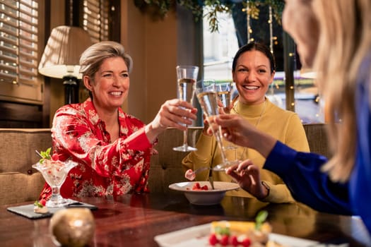 Small group of mature female friends making a celebratory toast while sitting around a table in a restaurant.