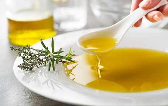 Healthy olive oil with herbs pouring with spoon close up