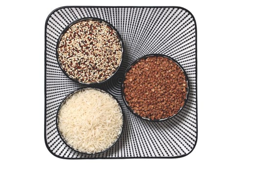 Vegetable food. Macro of a decorative plate with three bowls with buckwheat, rice and quinoa isolated on a white background. Healthy eating. Top view.