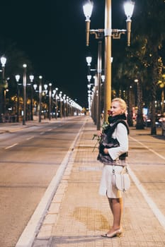 Beautiful woman holding a rose on a city street at night