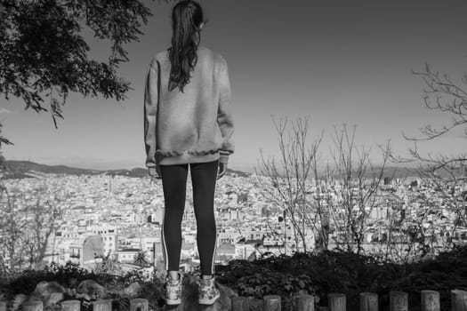Back view of the young girl enjoying the view of the city of Barcelona from the gardens dedicated to the poet Jacinto Verdaguer, Montjuic, Spain.