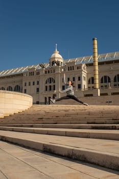 A young attractive girl makes a dance jumps leap along the staircase leading to the "Estadi Olímpic Lluís Companys"", Barcelona, Spain"