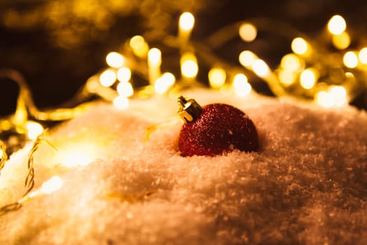 red Christmas ball and luminous garland on the snow.