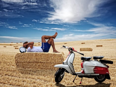Man lying on bale of hay next to his italian scooter