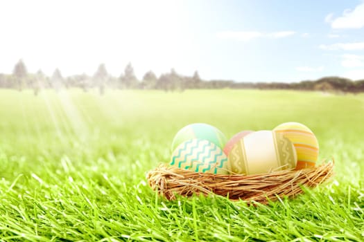 Colorful easter eggs in the nest on the grass field with trees and blue sky background. Happy Easter