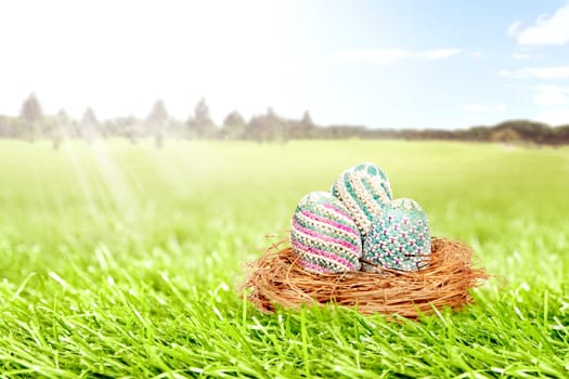 Colorful easter eggs in the nest on grass field with trees and blue sky background. Happy Easter