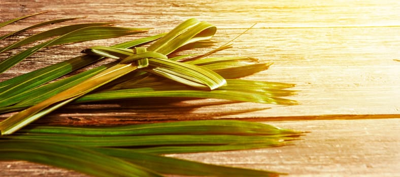 Closeup view of cross shape of palm leaf and palm branches with ray in wooden background. Palm Sunday concept