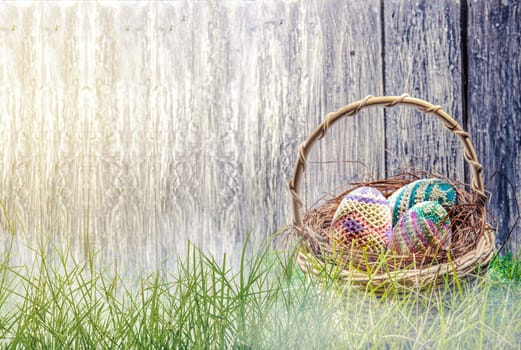 Colorful easter eggs in the nest on wooden basket at green grass with  fog and wooden fence background. Happy Easter