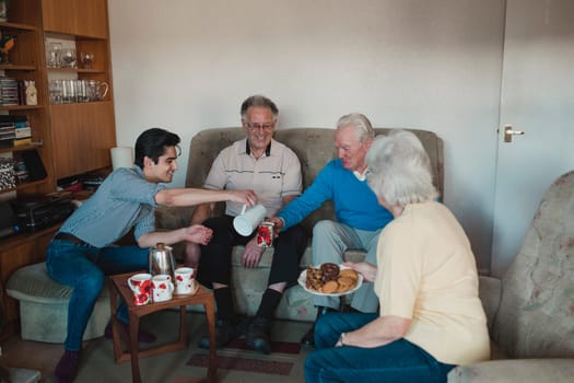 Teenage boy is assisting senior adults having a tea party at a nursing home.