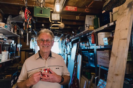 Portrait of a cheerful senior man in his workshop shed with a cup of tea.