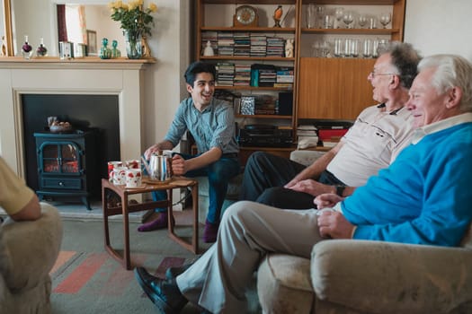 Teenage boy is assisting senior adults having a tea party at a nursing home.
