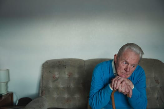 Portrait of a senior man looking sad while leaning on his walking stick.