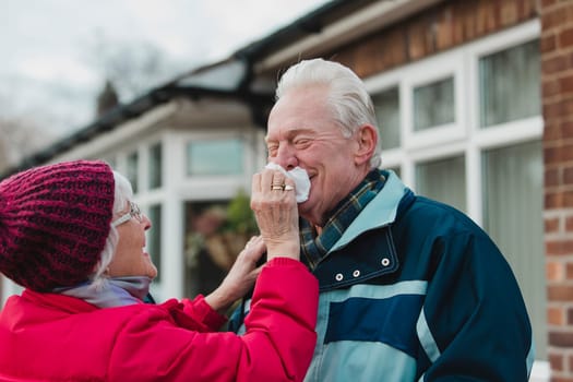 Senior woman is wiping her husbands nose while they are outside in the cold.