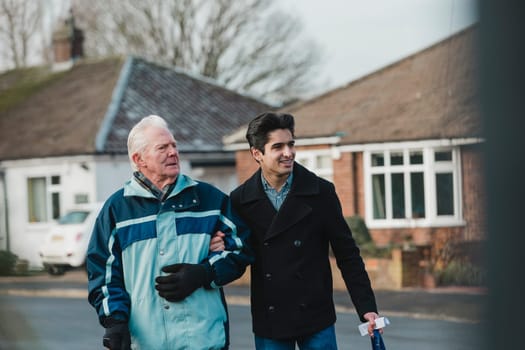Teenage boy is walking back from the shop with his grandparent. He is carrying the shopping bag and they are linking arms.