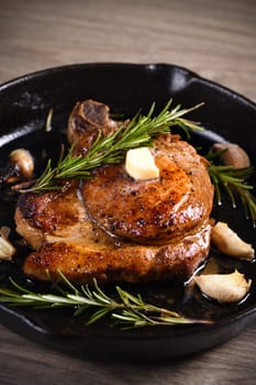 Pork cutlet on the bone in a piece of butter with garlic and rosemary in a frying pan 
