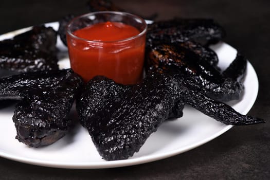 Bat wings. Cooked in sweet and sour sauce with cuttlefish ink, served with ketchup on a plate. An original idea for a Halloween party
