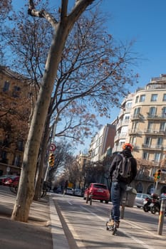 Young man in casual wear driving on electric push scooter on the fast lane of the city, Barcelona, Spain. Ecology transport concept.